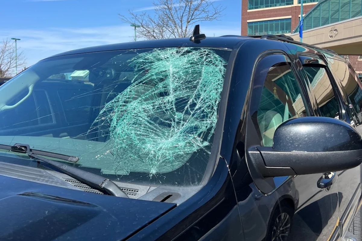 A black SUV with a severely shattered windshield parked in front of a commercial building, highlighting the potential cost and urgency of windshield repair in 2025.