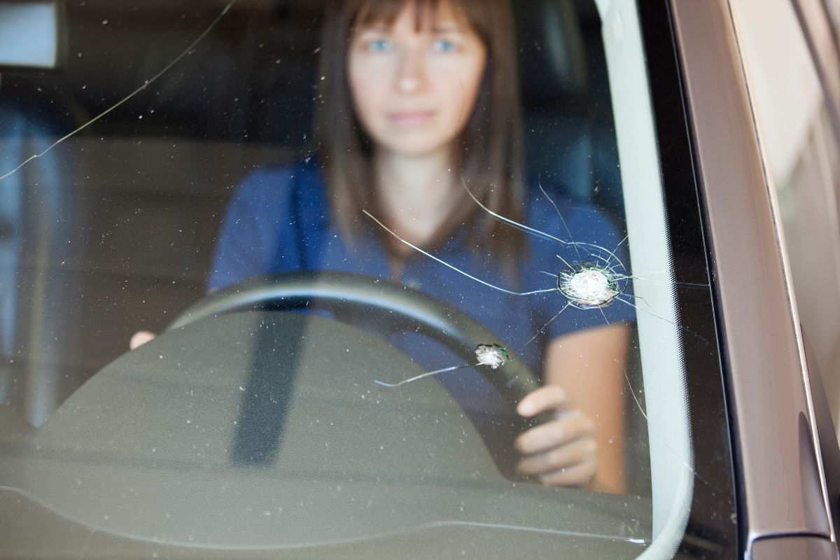 Woman driving with a chipped and cracked windshield, showing warning signs for replacement