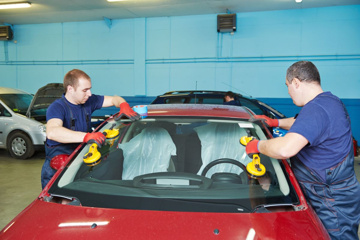 Technicians installing a new windshield on a car at an auto glass service center