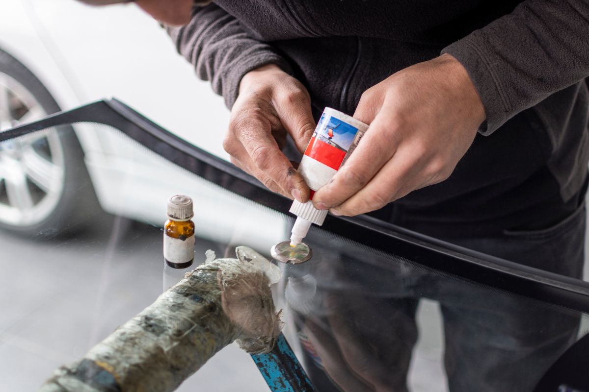 Close-up of a person applying glue to a chipped windshield, illustrating a risky DIY windshield repair attempt.