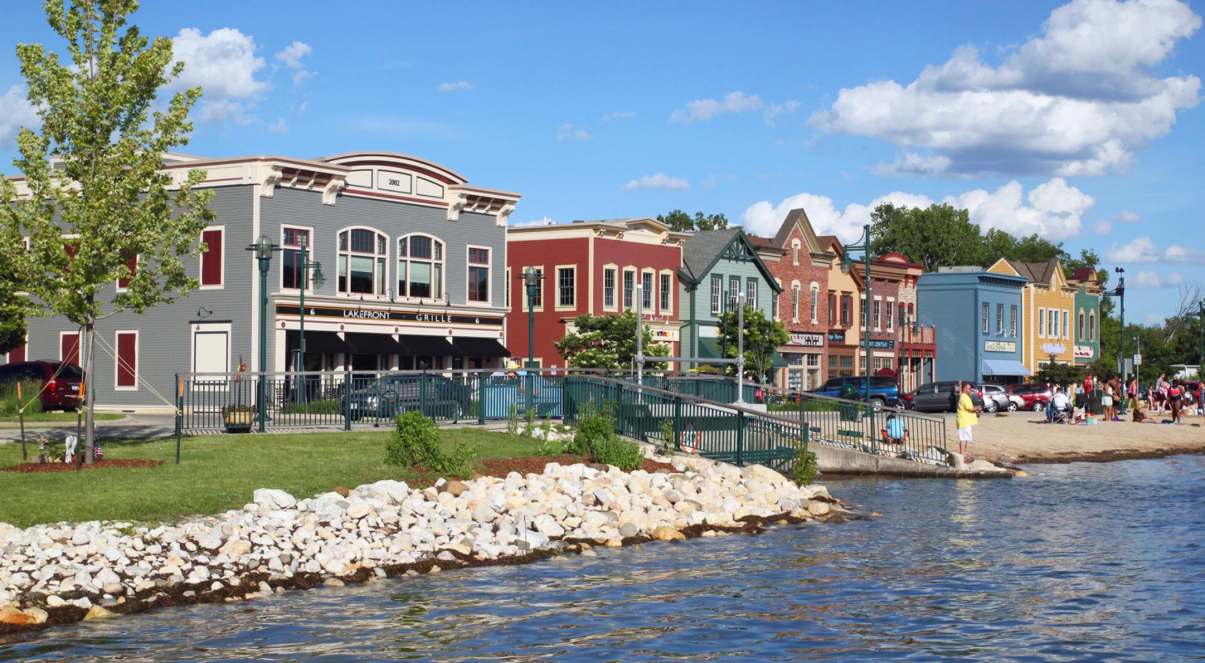 Downtown Pewaukee, WI view from the lakefront showing colorful shops and waterfront promenade on a sunny day