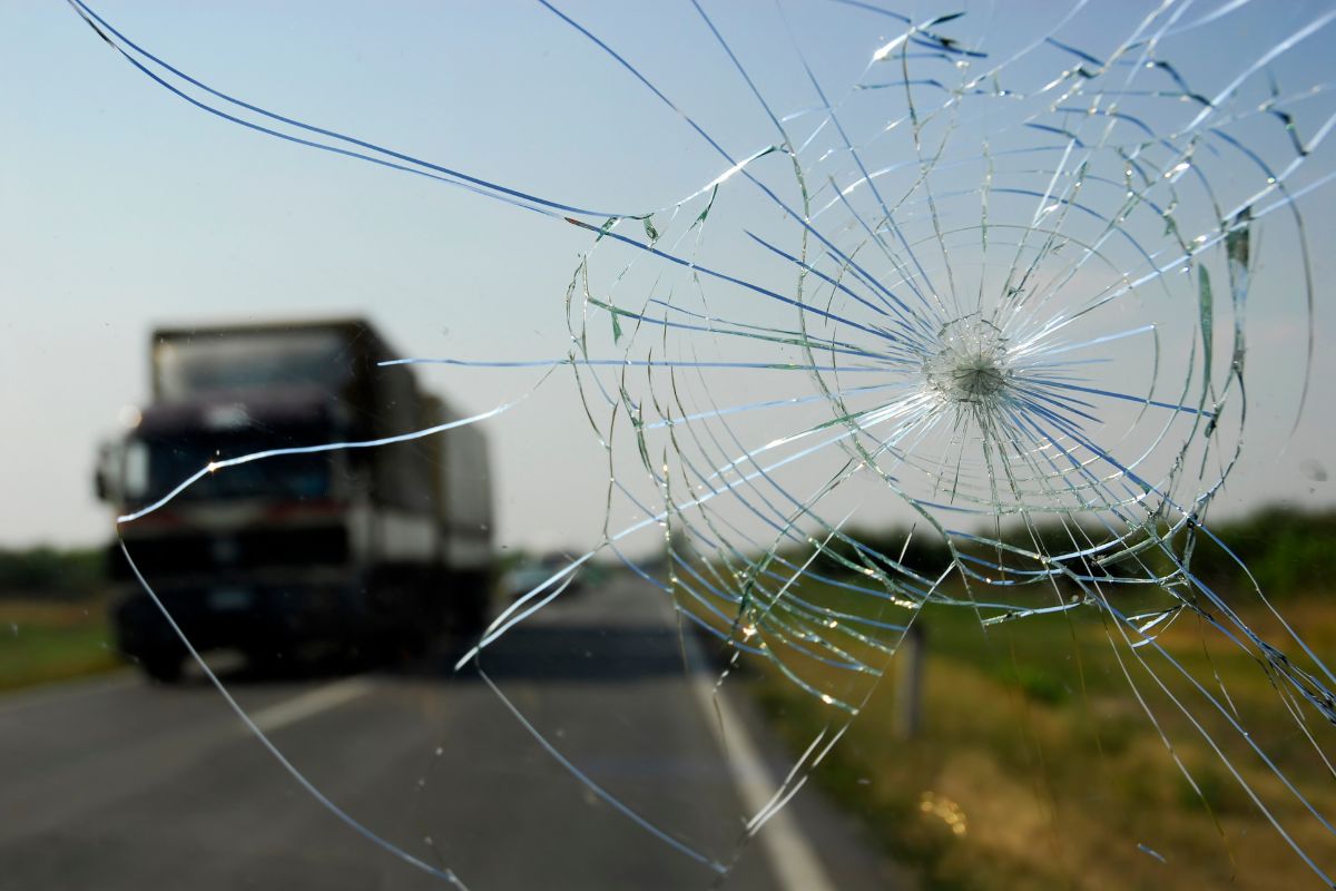Close-up of a cracked windshield on a Wisconsin road with salt and debris, illustrating common auto glass issues and the need for mobile repair.