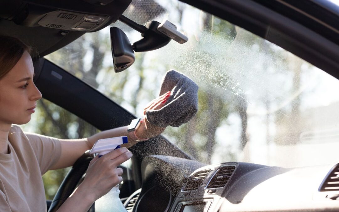Driver cleaning a windshield with a microfiber towel and cleaner, showing the best way to clean windshield without streaks – clear glass with sun reflecting off it.