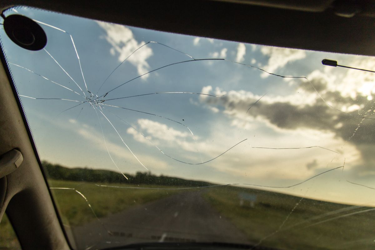 Cracked windshield with multiple long cracks spreading outward while driving on a rural Wisconsin road at sunset.