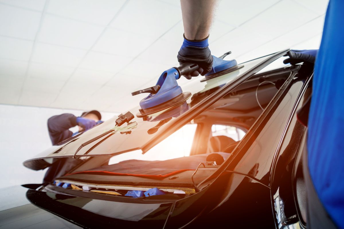 Technician installing a rear windshield on a black vehicle using suction cup tools, highlighting professional auto glass replacement services in Wisconsin.