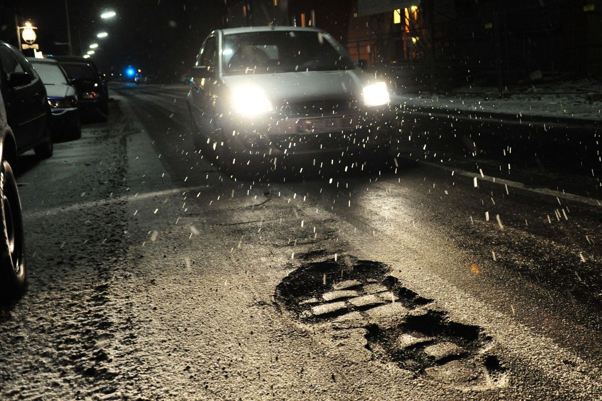 Car driving on a Wisconsin road with potholes that can cause windshield and auto glass damage.