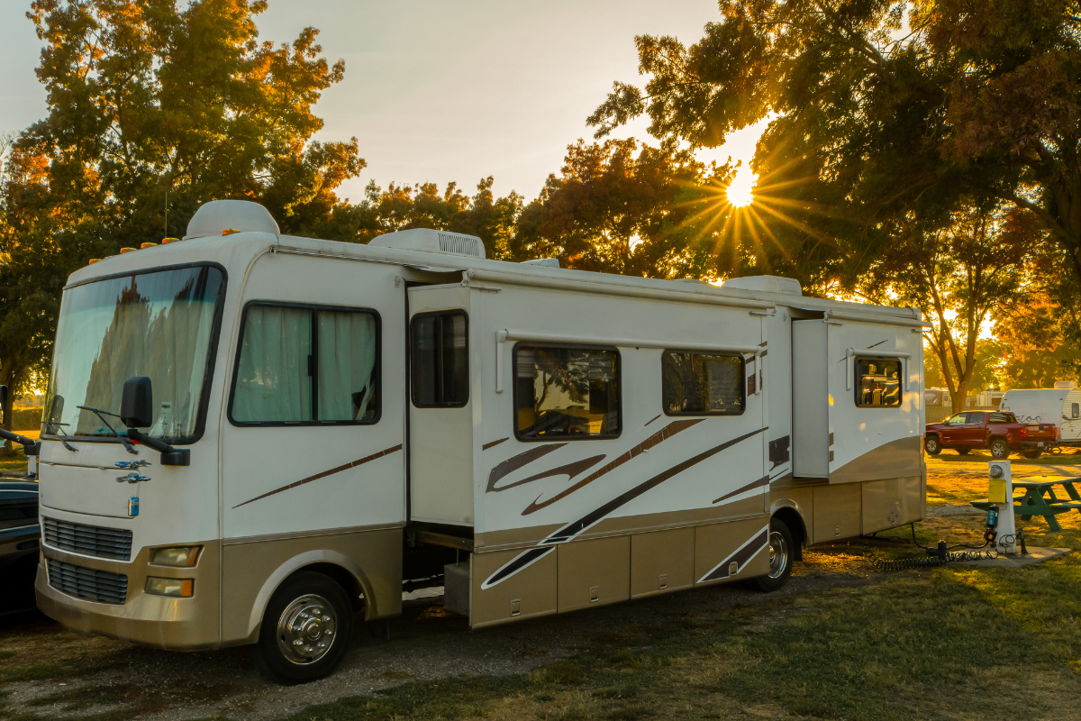 A large white and beige RV parked under trees at sunset, symbolizing custom RV glass cutting and replacement services for unique RV models in Wisconsin.