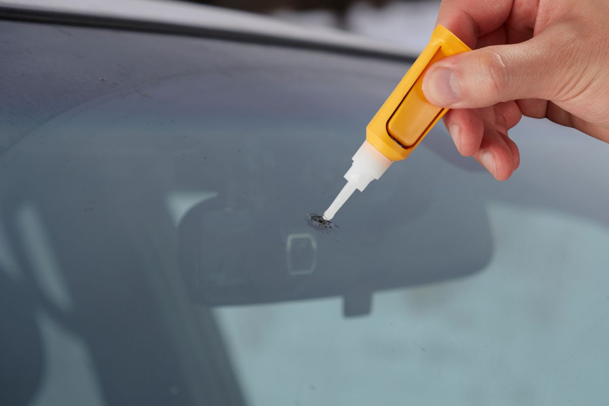 Hand applying glue to a cracked windshield in Wisconsin as a temporary DIY fix before professional auto glass repair.