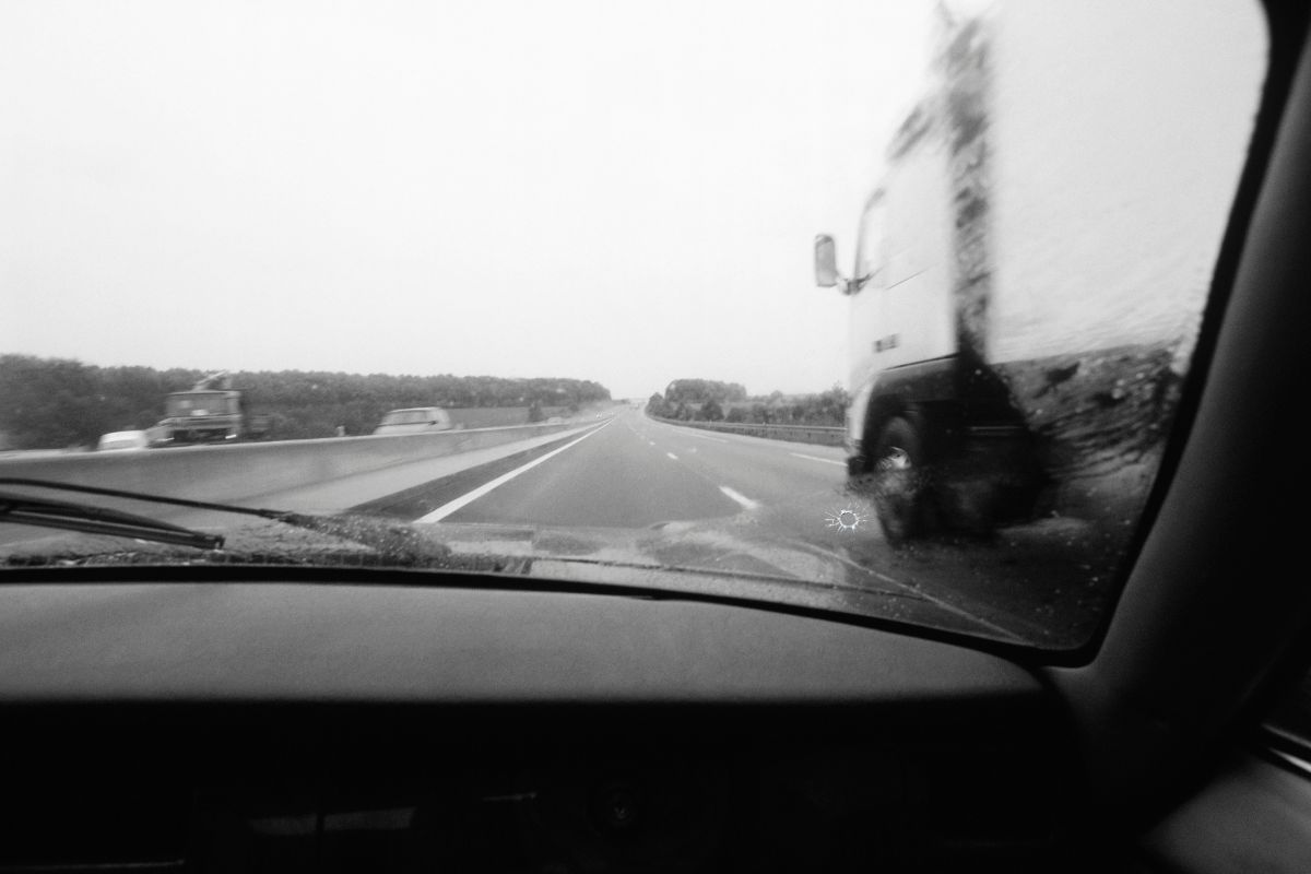 View from inside a car driving on I-94 with a small chip on the windshield, showing how road debris from nearby trucks can cause damage and highlight the importance of mobile windshield chip repair for Wisconsin commuters.