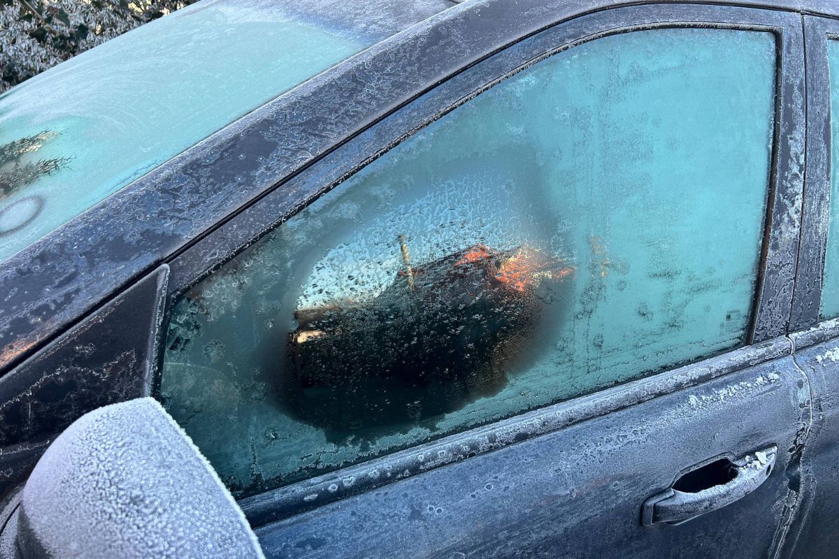 Car door and windows covered in heavy frost during winter, showing frozen glass and icy buildup on the exterior of the vehicle.