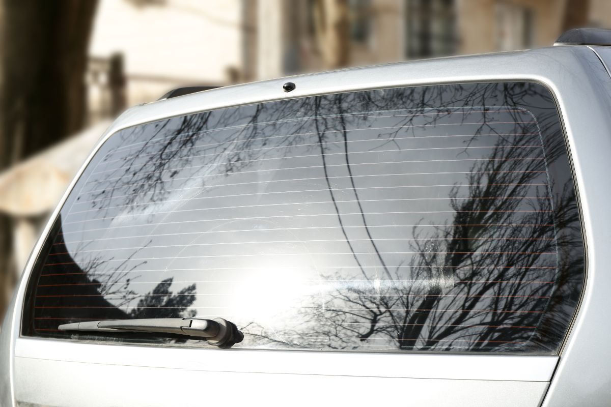 Rear window glass on a vehicle showing heating defroster lines, highlighting the condition of rear glass that may need replacement for visibility and safety.