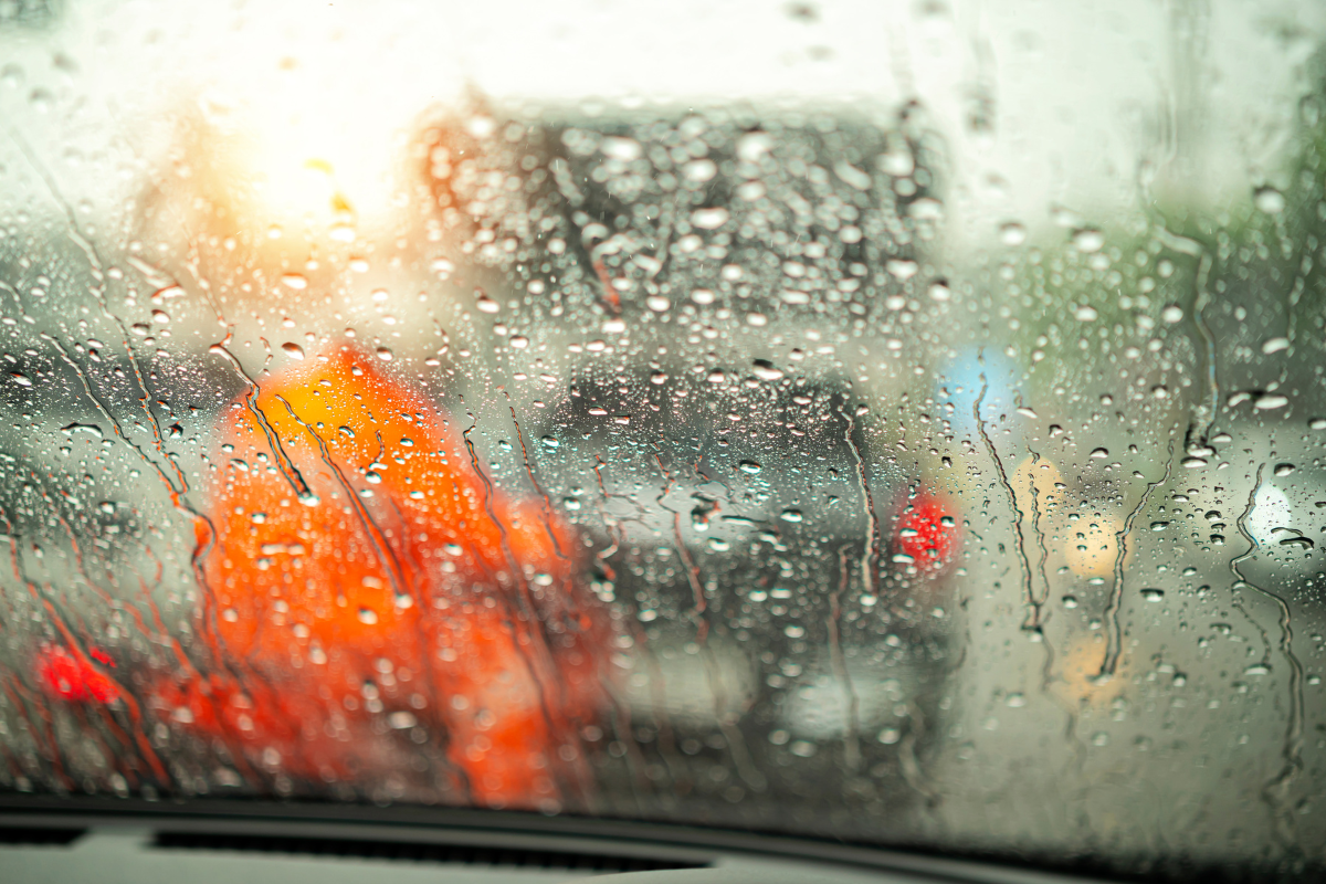Raindrops and water streaks on a car windshield, illustrating visibility issues and interior moisture caused by windshield leaks.